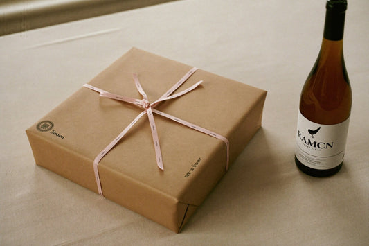 Ingepakt cadeau met lint naast een fles witte wijn